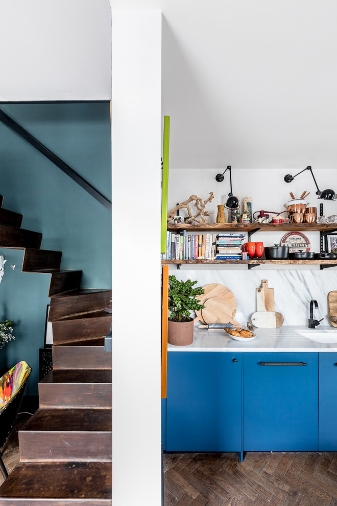 This is an example of a small eclectic single-wall kitchen/diner in London with a submerged sink, flat-panel cabinets, blue cabinets, marble worktops, white splashback, marble splashback, stainless steel appliances, medium hardwood flooring, brown floors and white worktops.