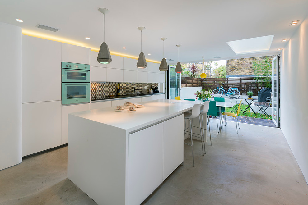 Inspiration for a mid-sized contemporary galley concrete floor and gray floor eat-in kitchen remodel in London with flat-panel cabinets, white cabinets, multicolored backsplash, colored appliances, an island, a double-bowl sink, solid surface countertops and white countertops