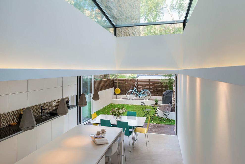 Medium sized contemporary single-wall open plan kitchen in London with a double-bowl sink, flat-panel cabinets, composite countertops, multi-coloured splashback, cement tile splashback, coloured appliances, concrete flooring, an island, grey floors and black worktops.