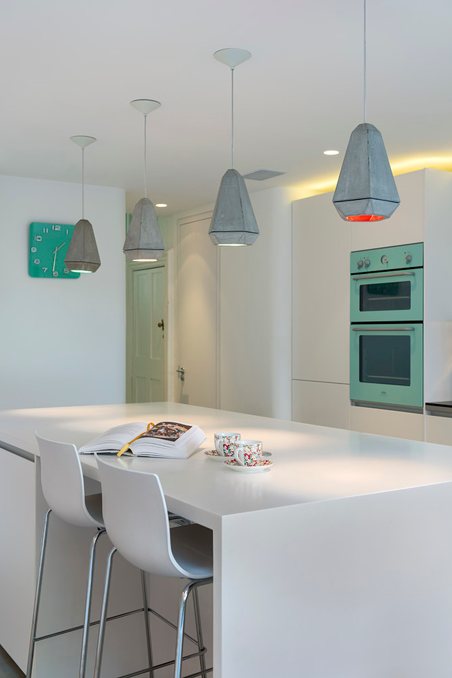 This is an example of a medium sized contemporary galley kitchen/diner in London with a double-bowl sink, flat-panel cabinets, white cabinets, composite countertops, multi-coloured splashback, coloured appliances, concrete flooring, an island, grey floors and white worktops.