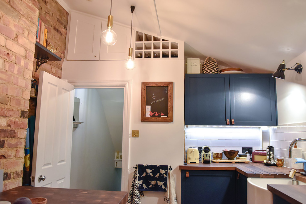 ロンドンにあるラグジュアリーな中くらいなモダンスタイルのおしゃれなキッチン (エプロンフロントシンク、シェーカースタイル扉のキャビネット、青いキャビネット、木材カウンター、白いキッチンパネル、セラミックタイルのキッチンパネル、黒い調理設備、セラミックタイルの床) の写真