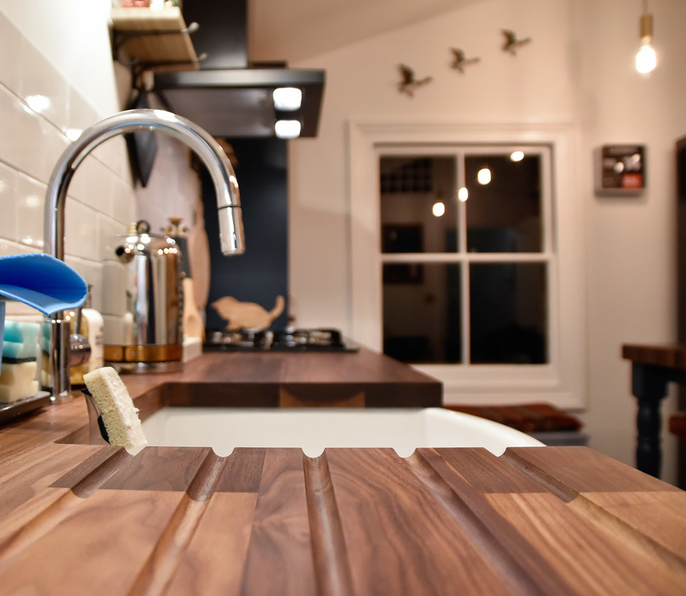 Foto på ett mellanstort funkis kök, med en rustik diskho, skåp i shakerstil, blå skåp, träbänkskiva, vitt stänkskydd, stänkskydd i keramik, svarta vitvaror, klinkergolv i keramik och en halv köksö