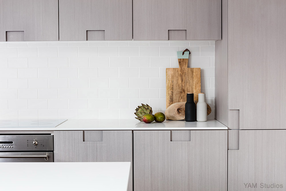 This is an example of a small scandi u-shaped open plan kitchen in London with a built-in sink, flat-panel cabinets, light wood cabinets, composite countertops, white splashback, ceramic splashback, stainless steel appliances, light hardwood flooring and no island.