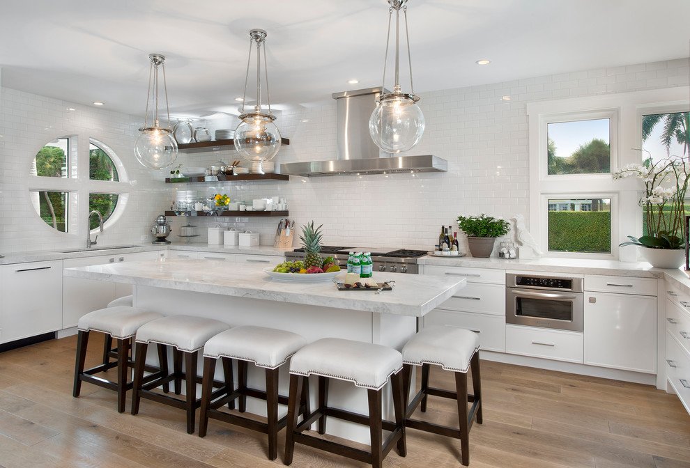Modern inredning av ett u-kök, med en undermonterad diskho, luckor med profilerade fronter, vita skåp, marmorbänkskiva, vitt stänkskydd, stänkskydd i tunnelbanekakel, rostfria vitvaror, ljust trägolv och en köksö