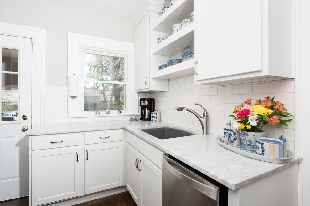 Bild på ett litet kök, med en enkel diskho, skåp i shakerstil, vita skåp, marmorbänkskiva, vitt stänkskydd, stänkskydd i tunnelbanekakel, rostfria vitvaror och mellanmörkt trägolv