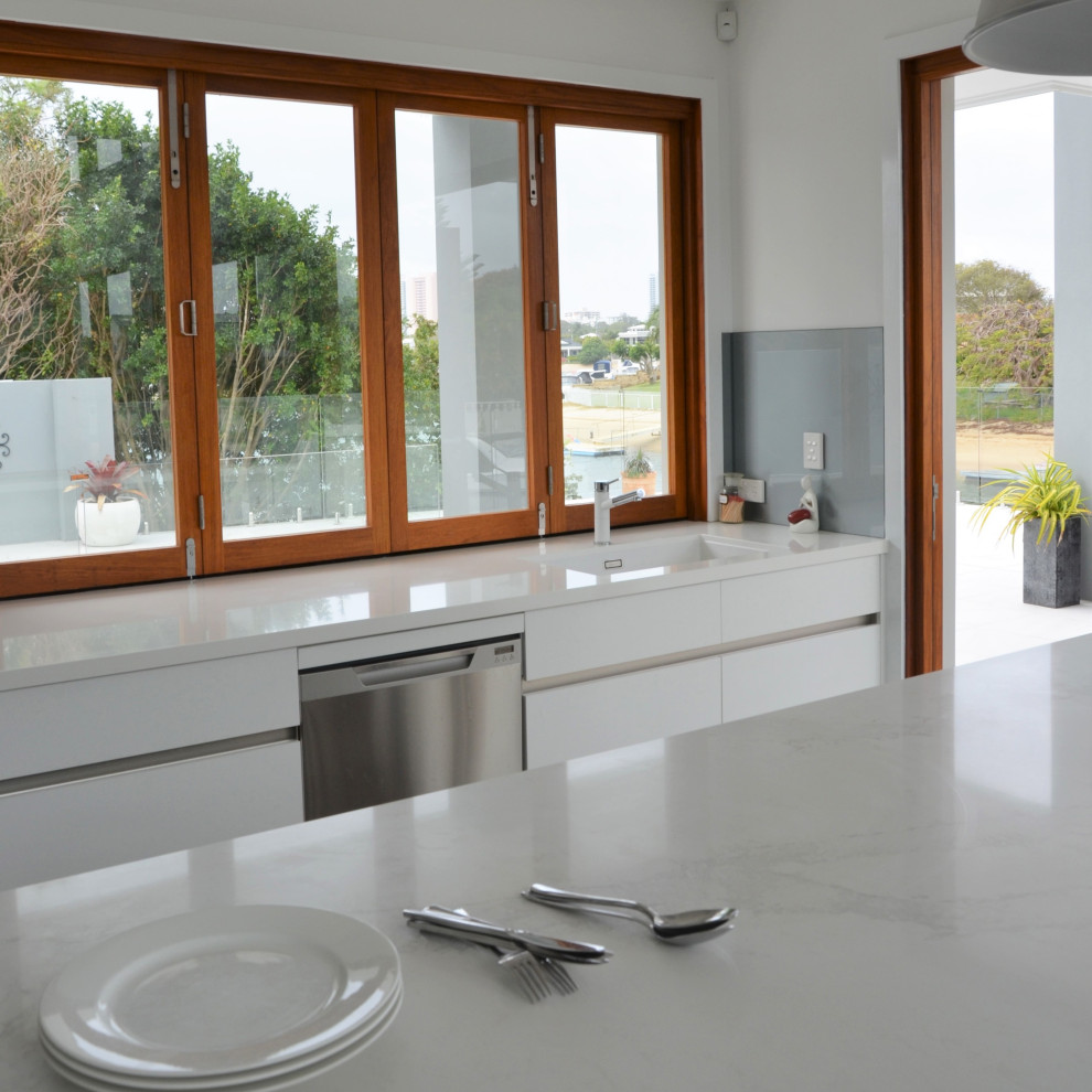 Exempel på ett mellanstort modernt vit vitt kök och matrum, med en undermonterad diskho, släta luckor, vita skåp, bänkskiva i kvarts, blått stänkskydd, glaspanel som stänkskydd, klinkergolv i keramik, en köksö och grått golv