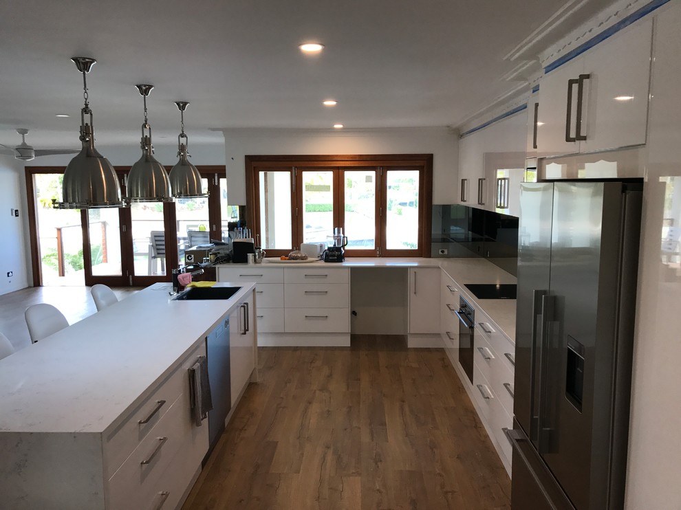 Inredning av ett modernt mellanstort kök, med vita skåp, bänkskiva i kvarts, stänkskydd i metallkakel, laminatgolv, en köksö och brunt golv