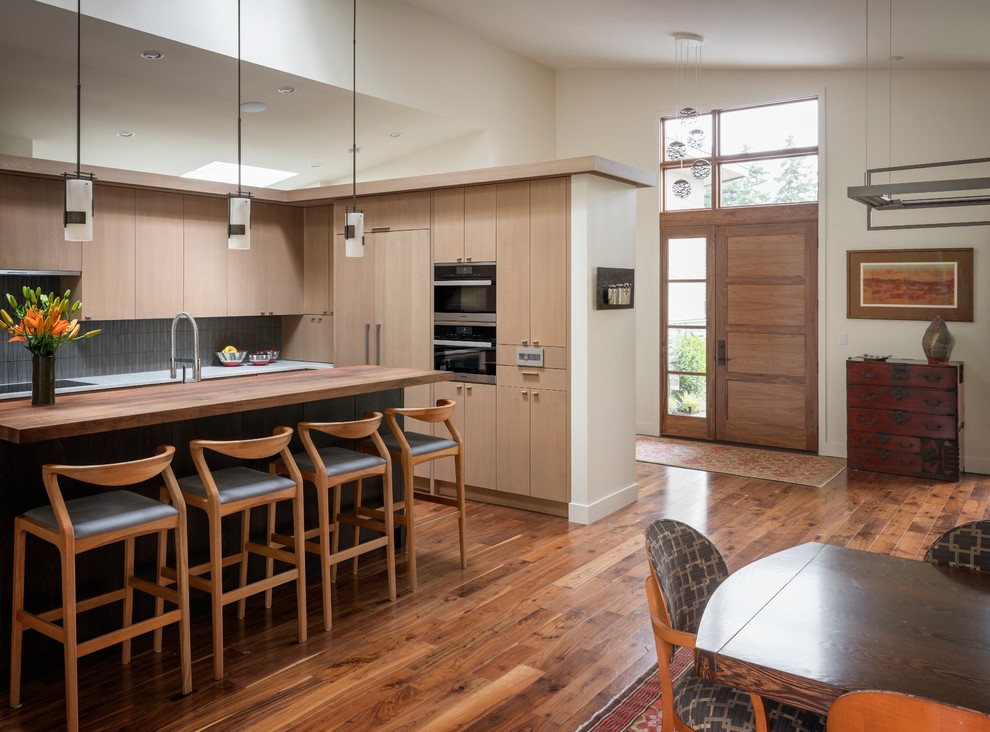 This is an example of a contemporary u-shaped open plan kitchen in Seattle with a single-bowl sink, flat-panel cabinets, light wood cabinets, engineered stone countertops, glass tiled splashback, integrated appliances, medium hardwood flooring, an island, brown floors and white worktops.