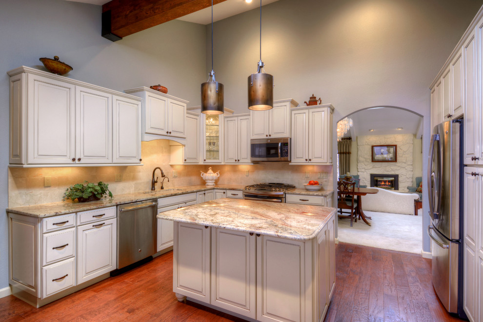 Example of a large classic l-shaped medium tone wood floor enclosed kitchen design in Denver with an undermount sink, granite countertops, beige backsplash, stone tile backsplash, stainless steel appliances, an island, raised-panel cabinets and beige cabinets