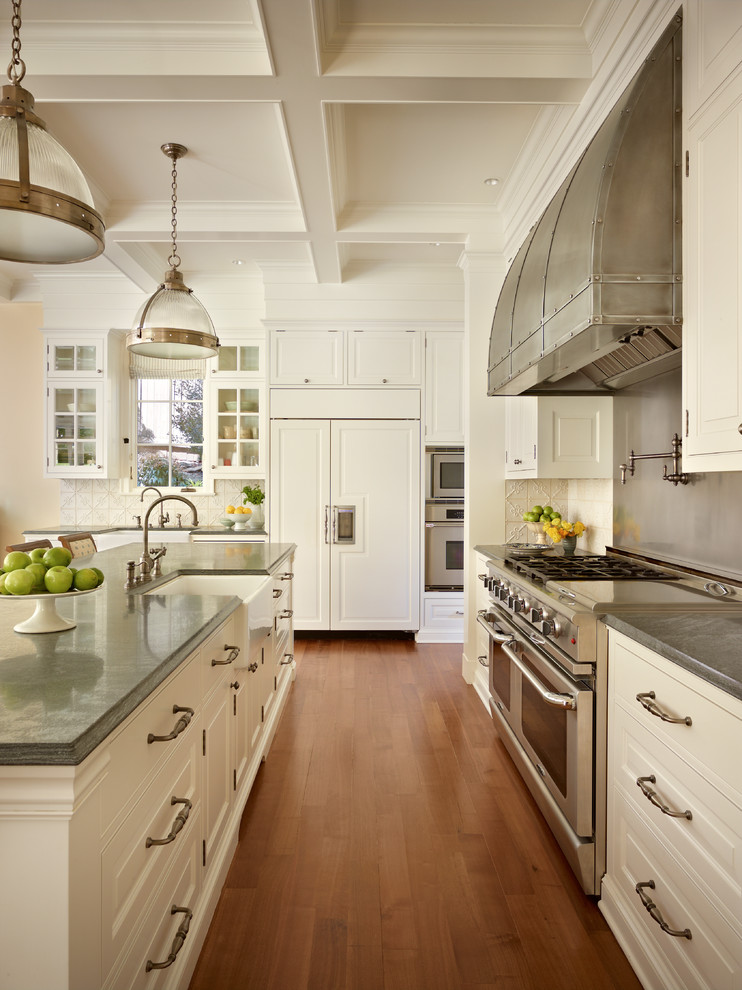 Example of a classic kitchen design in Seattle with a farmhouse sink, raised-panel cabinets, white cabinets, white backsplash and stainless steel appliances