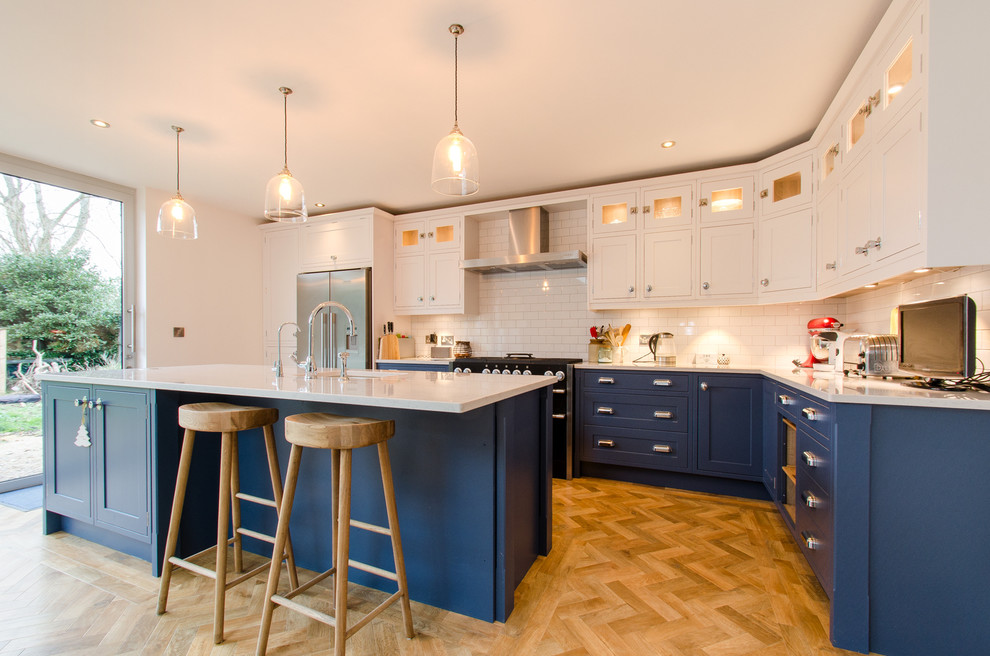 Large country l-shaped kitchen/diner in Kent with an integrated sink, shaker cabinets, blue cabinets, quartz worktops, metro tiled splashback, coloured appliances, medium hardwood flooring and an island.