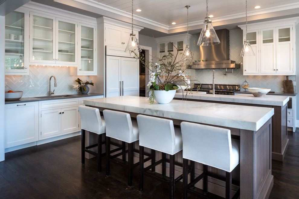 Inspiration for a large timeless dark wood floor and brown floor open concept kitchen remodel in New York with a farmhouse sink, shaker cabinets, white cabinets, white backsplash, ceramic backsplash, paneled appliances and two islands