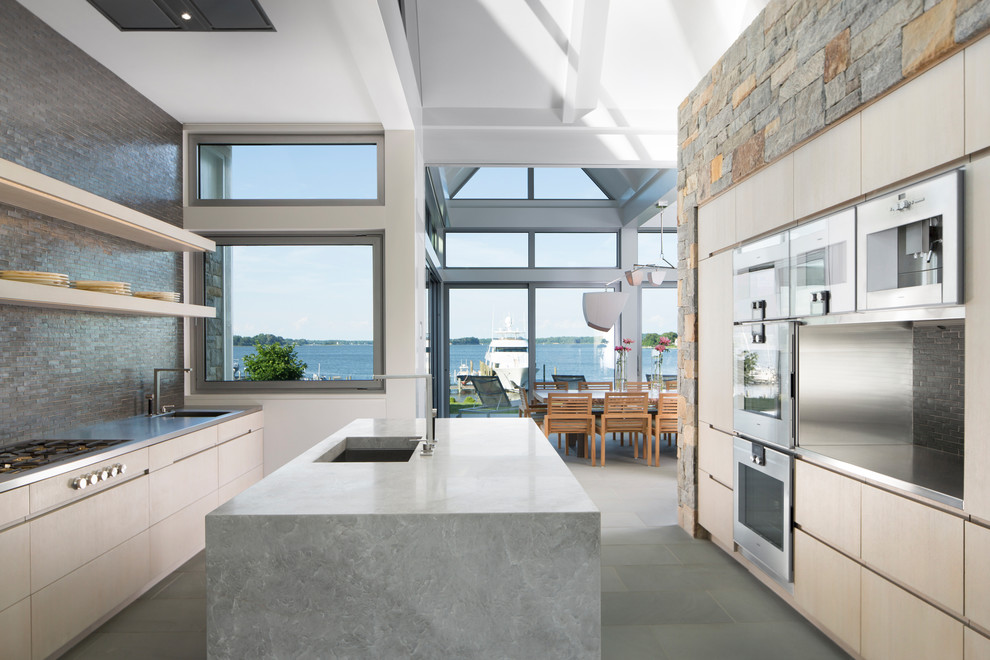 Photo of a coastal galley kitchen in DC Metro with a submerged sink, flat-panel cabinets, light wood cabinets, grey splashback, mosaic tiled splashback, stainless steel appliances and an island.