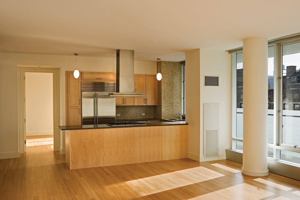 Cette image montre une petite cuisine ouverte parallèle design en bois clair avec un plan de travail en granite, une crédence verte, une crédence en carreau de verre, un électroménager en acier inoxydable, parquet clair et îlot.