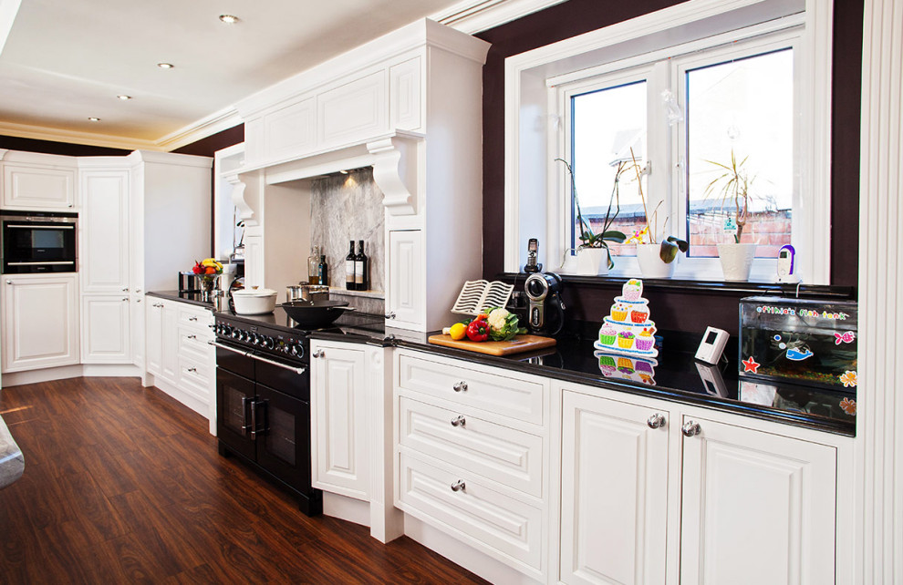 Immagine di un cucina con isola centrale minimal di medie dimensioni con ante in stile shaker, ante bianche, top in granito, pavimento marrone e top nero