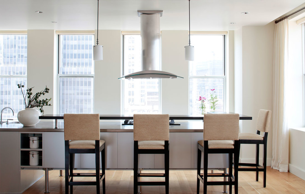 Foto de cocina contemporánea con electrodomésticos de acero inoxidable, suelo de madera clara, una isla y barras de cocina