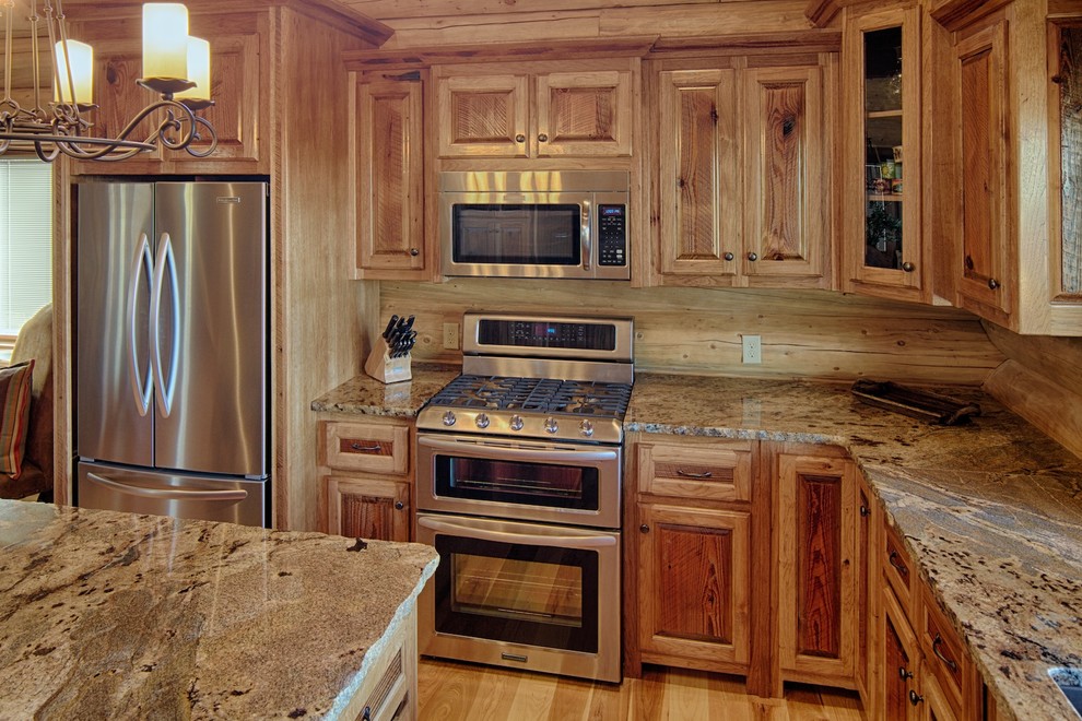 Modelo de cocina rústica de obra con armarios con paneles con relieve, encimera de granito, electrodomésticos de acero inoxidable y puertas de armario de madera oscura