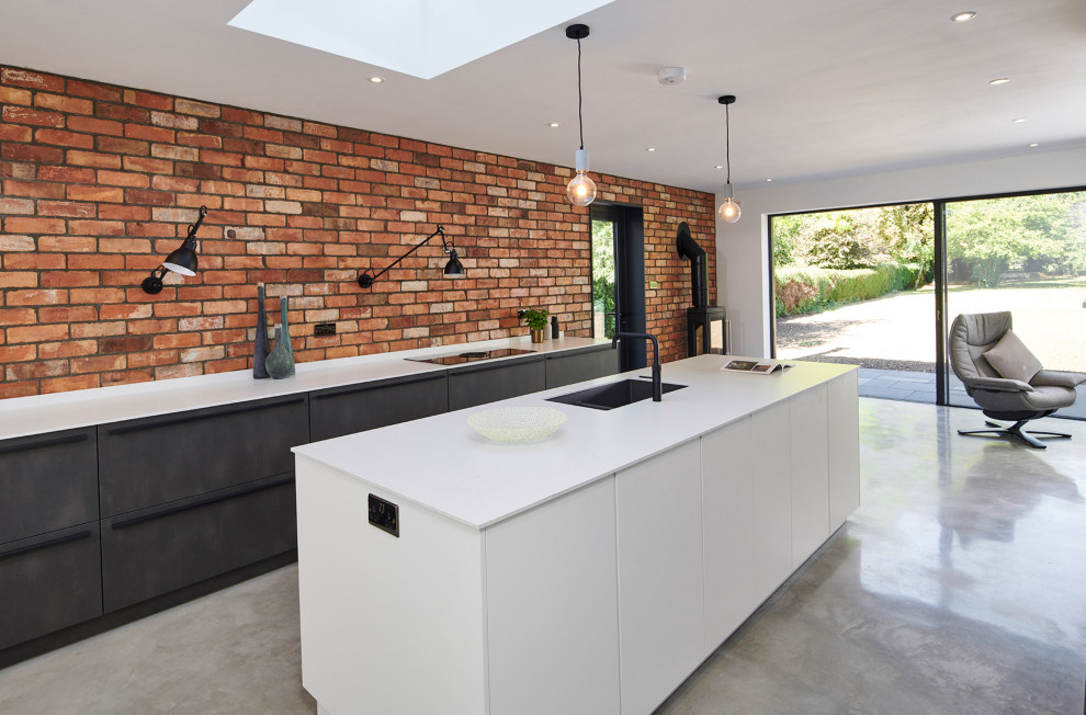 Inspiration for an urban open plan kitchen in Cambridgeshire with a single-bowl sink, flat-panel cabinets, black cabinets, brick splashback, concrete flooring, an island, grey floors and white worktops.