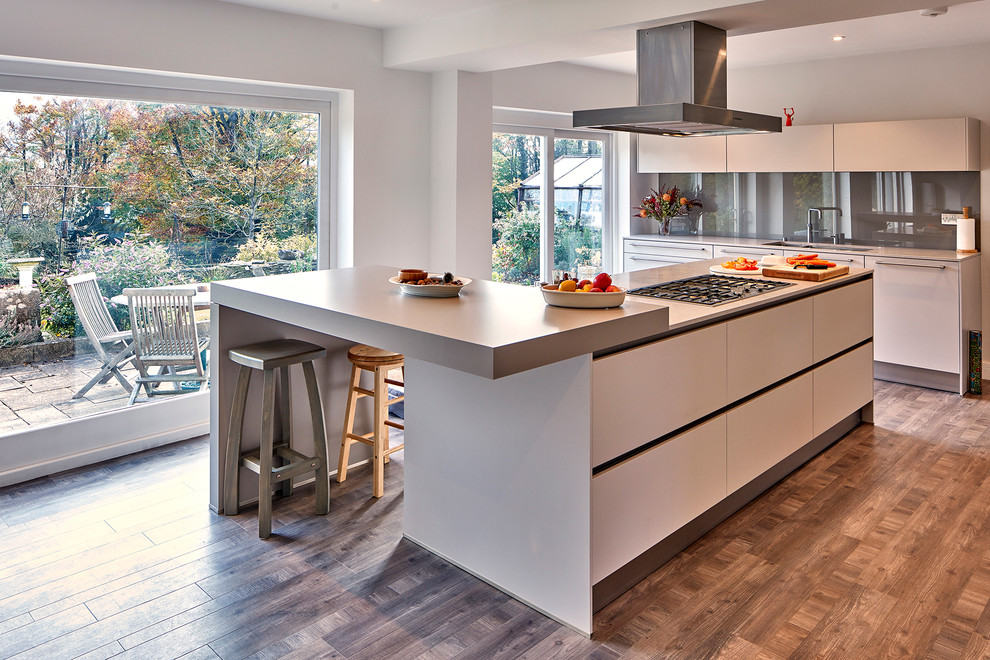 Foto på ett stort funkis linjärt kök och matrum, med en integrerad diskho, släta luckor, vita skåp, laminatbänkskiva, glaspanel som stänkskydd, mörkt trägolv, en köksö och brunt golv