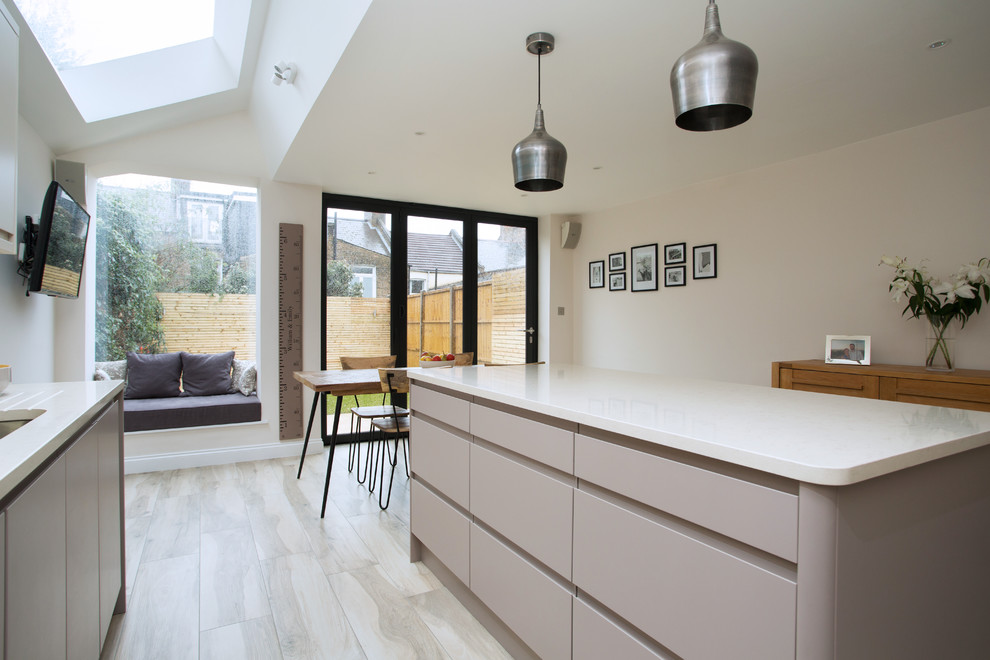 Large contemporary kitchen in London with flat-panel cabinets, beige cabinets, composite countertops, white splashback, ceramic flooring, an island and beige floors.