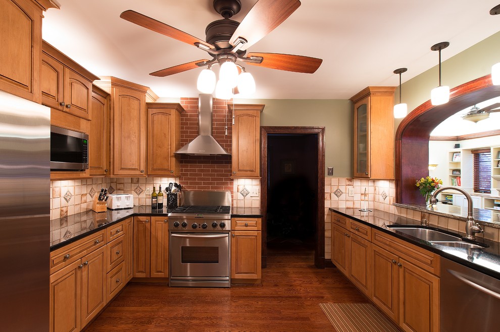 Klassisk inredning av ett avskilt, mellanstort u-kök, med en undermonterad diskho, luckor med upphöjd panel, skåp i mellenmörkt trä, granitbänkskiva, brunt stänkskydd, stänkskydd i keramik, rostfria vitvaror och mörkt trägolv