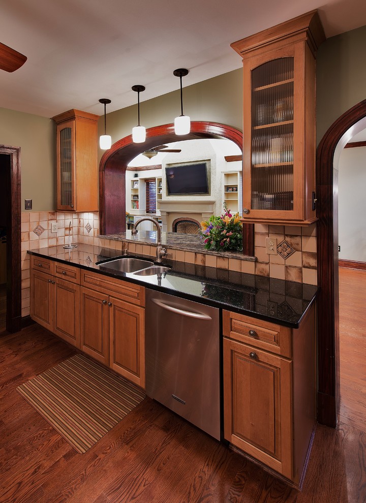 Klassisk inredning av ett avskilt, mellanstort u-kök, med en undermonterad diskho, luckor med upphöjd panel, skåp i mellenmörkt trä, granitbänkskiva, brunt stänkskydd, stänkskydd i keramik, rostfria vitvaror och mörkt trägolv