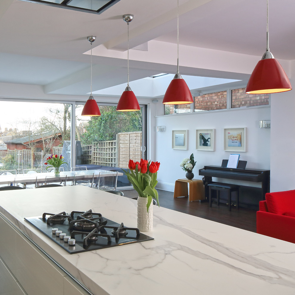 Exempel på ett stort modernt kök, med en integrerad diskho, släta luckor, vita skåp, granitbänkskiva, rött stänkskydd, glaspanel som stänkskydd, rostfria vitvaror, mörkt trägolv och en köksö
