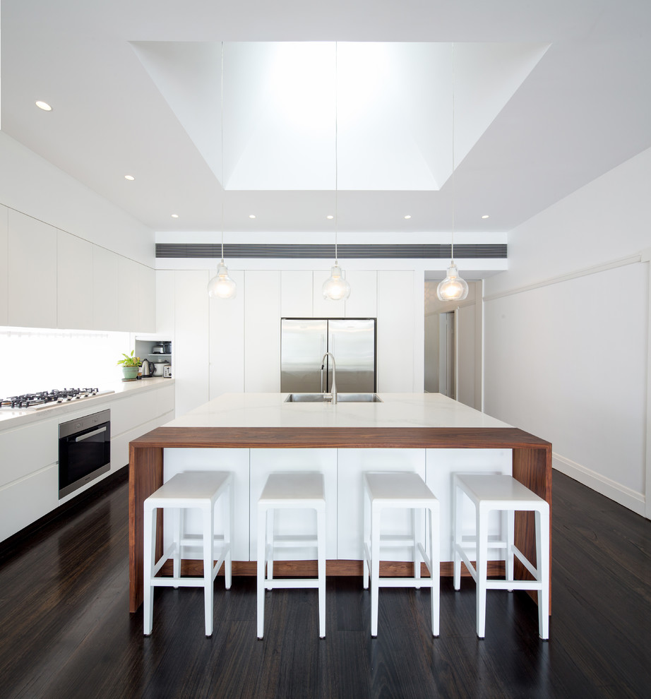 Moderne Küche in L-Form mit Unterbauwaschbecken, flächenbündigen Schrankfronten, weißen Schränken, Küchenrückwand in Weiß, dunklem Holzboden und Kücheninsel in Sonstige