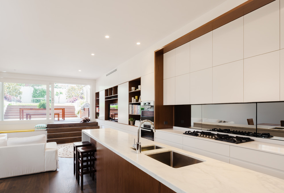 This is an example of a nautical galley kitchen/diner in Sydney with a submerged sink, marble worktops, mirror splashback, stainless steel appliances, dark hardwood flooring, an island, metallic splashback and brown floors.