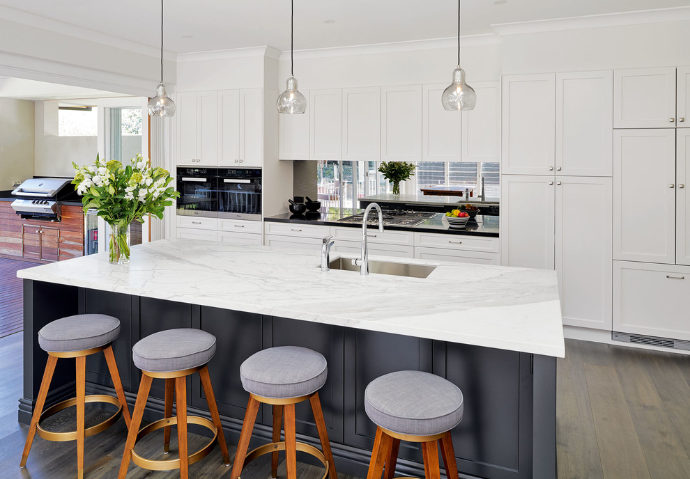 Design ideas for a large contemporary single-wall open plan kitchen in Sydney with a built-in sink, shaker cabinets, white cabinets, engineered stone countertops, metallic splashback, mirror splashback, stainless steel appliances, laminate floors, an island and brown floors.