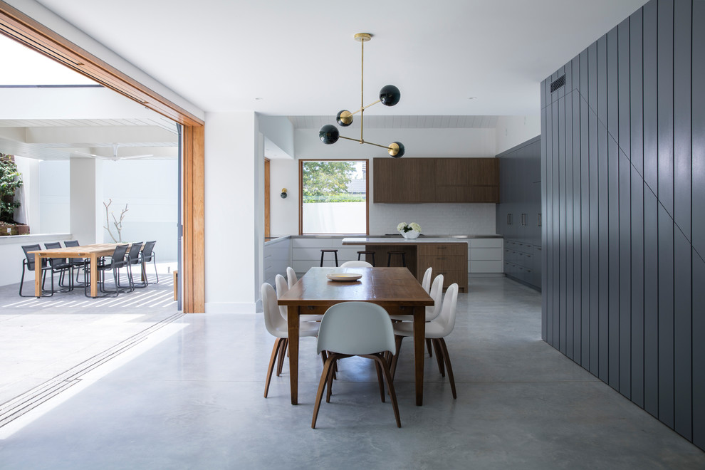This is an example of a beach style u-shaped kitchen/diner in Sydney with flat-panel cabinets, white cabinets, stainless steel worktops, white splashback, metro tiled splashback, concrete flooring, an island, grey floors and grey worktops.