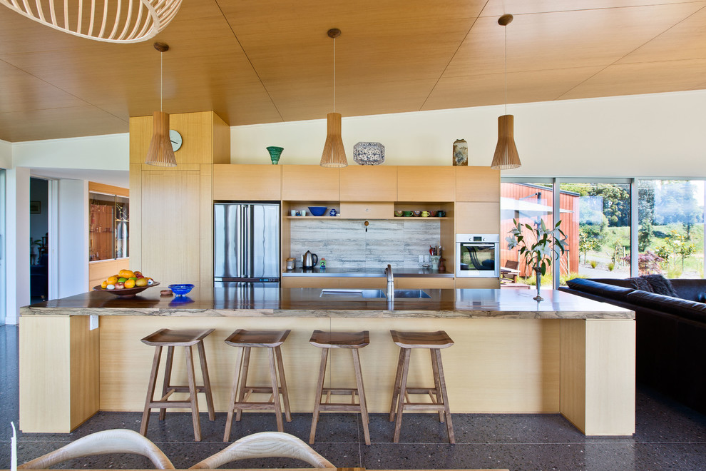Cette photo montre une cuisine ouverte parallèle tendance en bois clair avec un placard à porte plane, une crédence blanche, un électroménager en acier inoxydable et îlot.