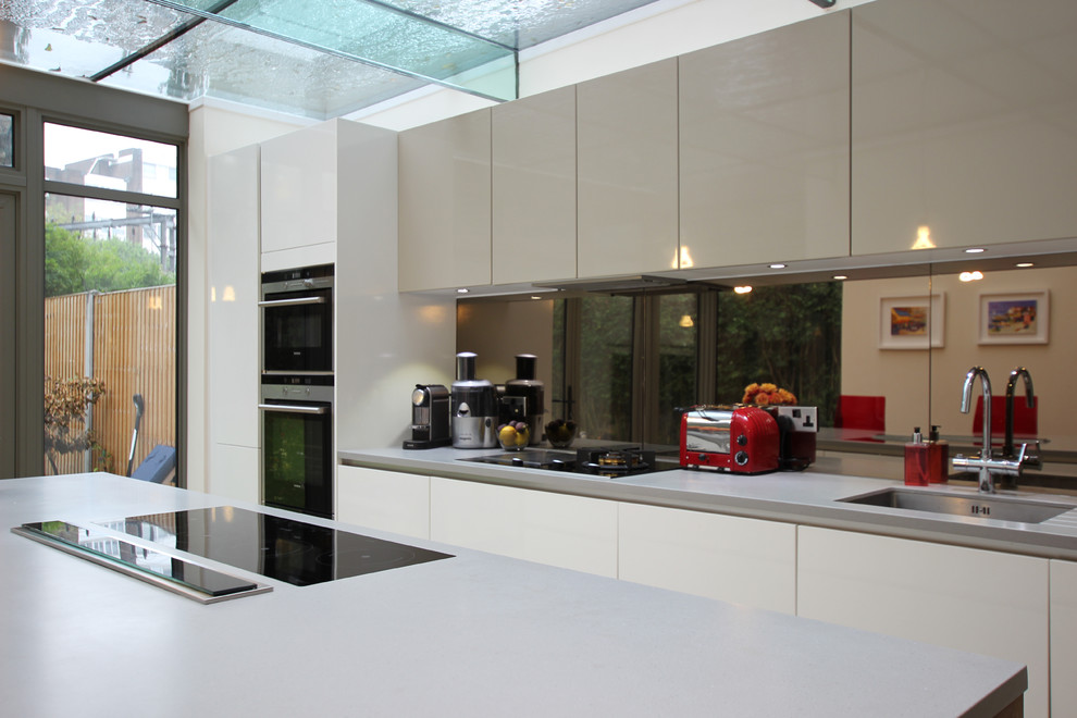 Trendy kitchen photo in London with mirror backsplash and an island