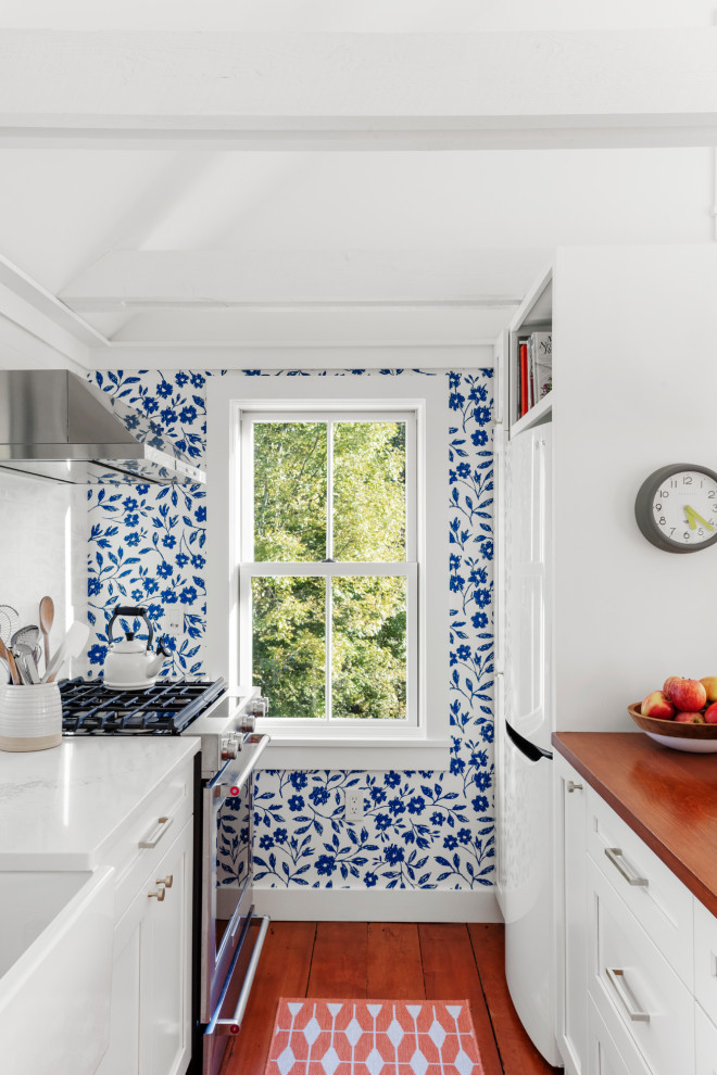 Skandinavisk inredning av ett litet vit vitt kök, med en rustik diskho, luckor med infälld panel, vita skåp, bänkskiva i kvartsit, vitt stänkskydd, rostfria vitvaror, mellanmörkt trägolv och en halv köksö
