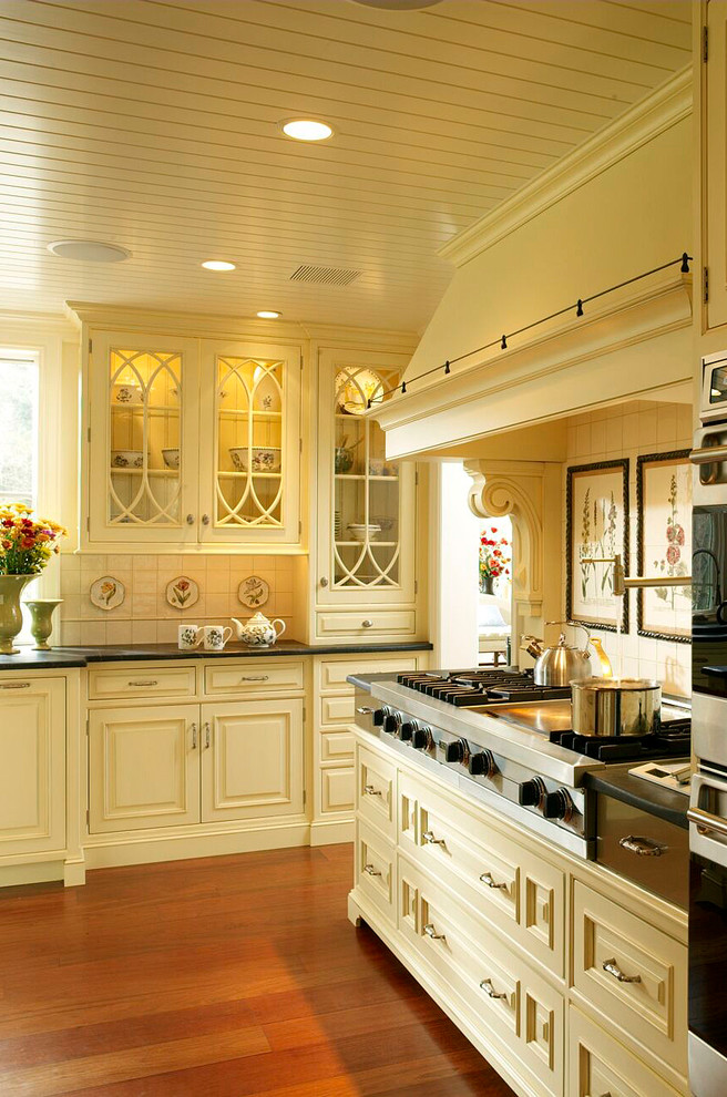 Klassisk inredning av ett avskilt l-kök, med en undermonterad diskho, luckor med profilerade fronter, gula skåp, bänkskiva i täljsten, gult stänkskydd, stänkskydd i keramik, rostfria vitvaror, mellanmörkt trägolv och en köksö