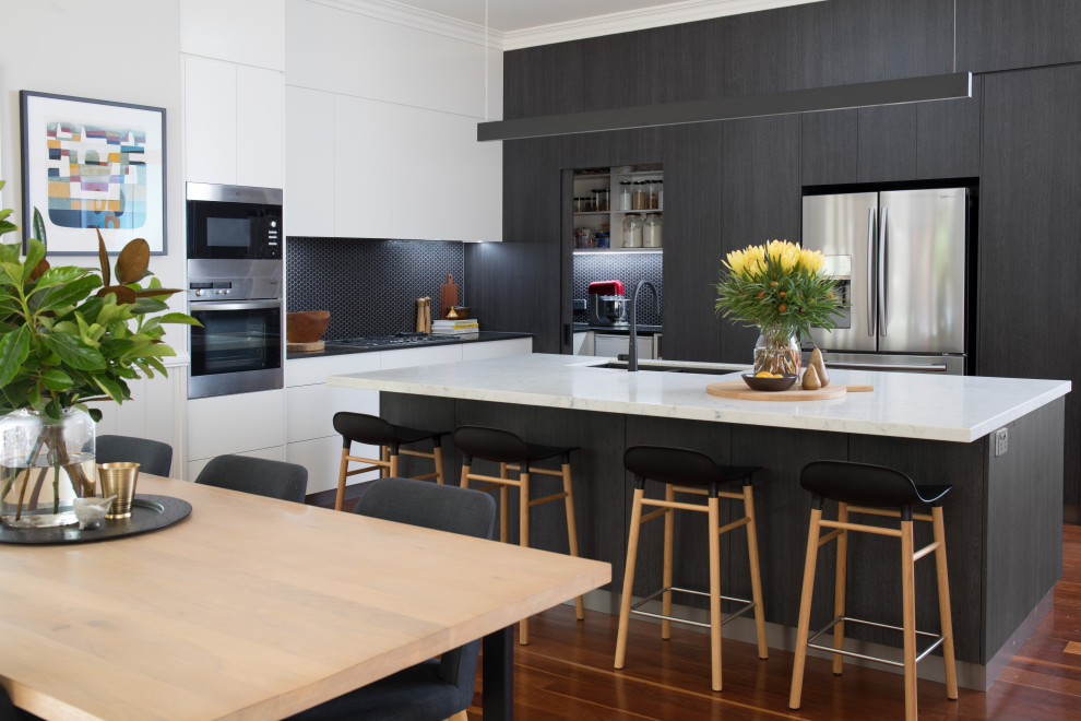Moderne Küche in L-Form mit Unterbauwaschbecken, flächenbündigen Schrankfronten, schwarzen Schränken, Küchenrückwand in Schwarz, Rückwand aus Mosaikfliesen, Küchengeräten aus Edelstahl, dunklem Holzboden, Kücheninsel, braunem Boden und weißer Arbeitsplatte in Brisbane