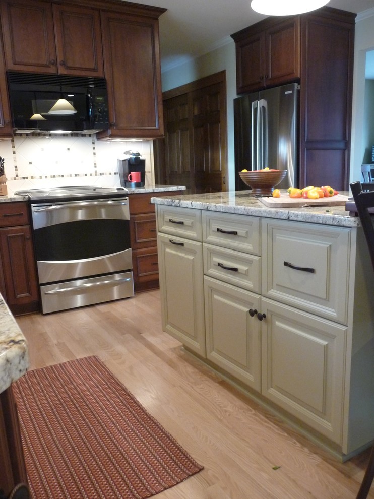 Klassisk inredning av ett kök, med en undermonterad diskho, luckor med infälld panel, skåp i mörkt trä, granitbänkskiva, vitt stänkskydd, stänkskydd i keramik, rostfria vitvaror, ljust trägolv och en köksö