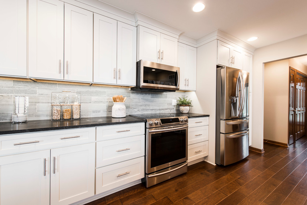 This is an example of a traditional single-wall kitchen/diner in Milwaukee with a submerged sink, shaker cabinets, white cabinets, soapstone worktops, grey splashback, stone tiled splashback, stainless steel appliances, dark hardwood flooring and an island.