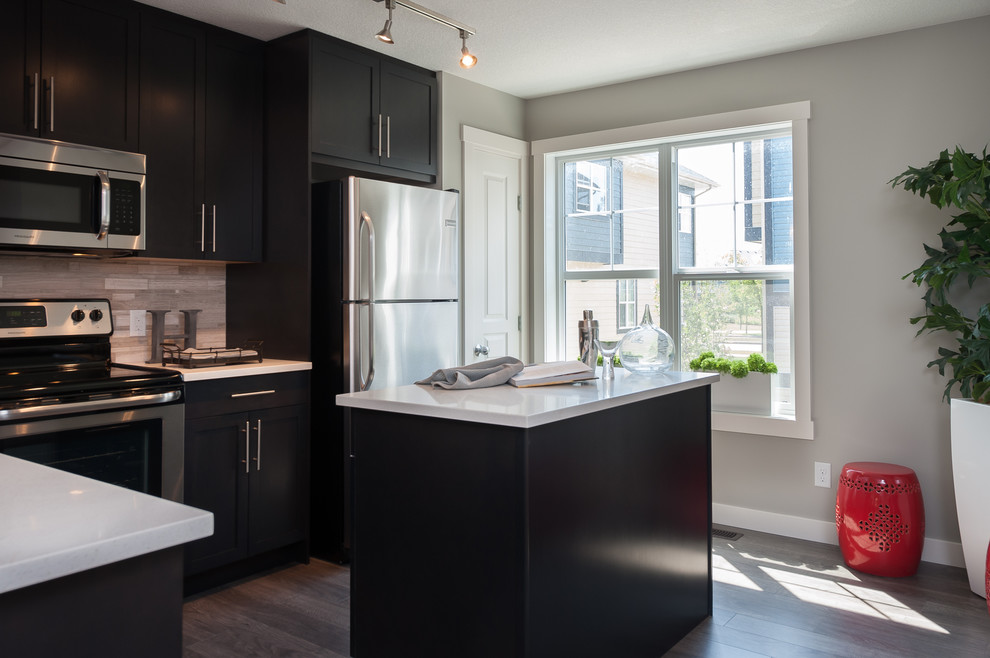 Kleine Moderne Wohnküche in L-Form mit Doppelwaschbecken, Schrankfronten mit vertiefter Füllung, dunklen Holzschränken, Quarzit-Arbeitsplatte, Küchenrückwand in Beige, Rückwand aus Stäbchenfliesen, Küchengeräten aus Edelstahl, hellem Holzboden und Kücheninsel in Calgary