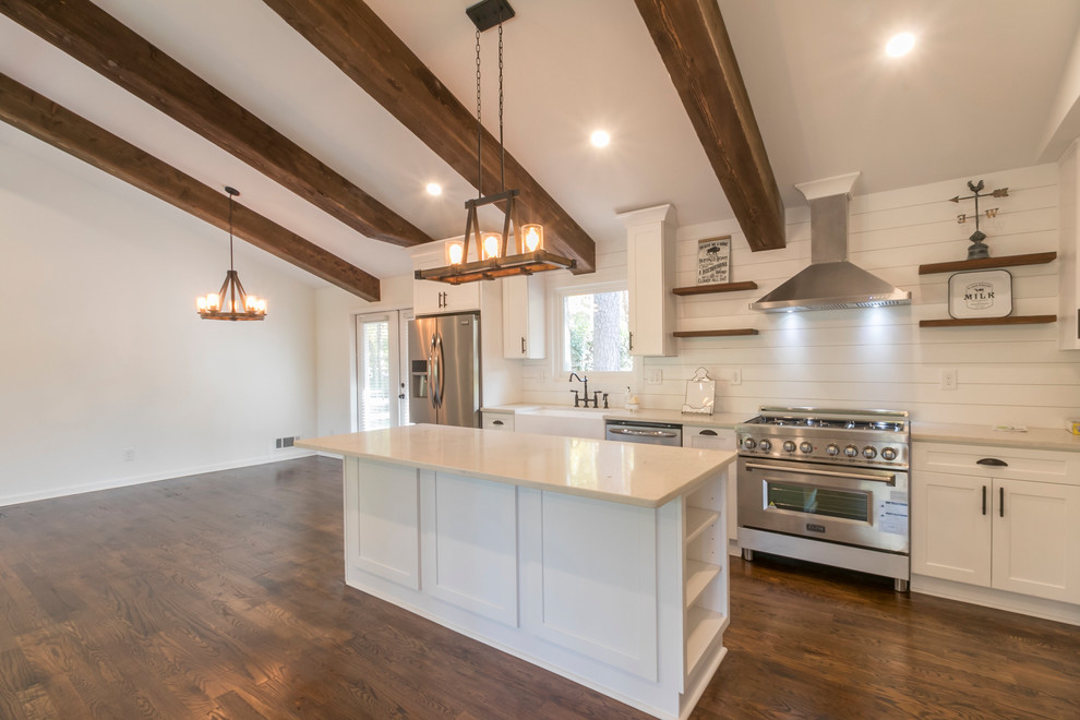 Mid-sized farmhouse l-shaped dark wood floor and brown floor open concept kitchen photo in Atlanta with a farmhouse sink, shaker cabinets, white cabinets, quartzite countertops, white backsplash, wood backsplash, stainless steel appliances, an island and white countertops