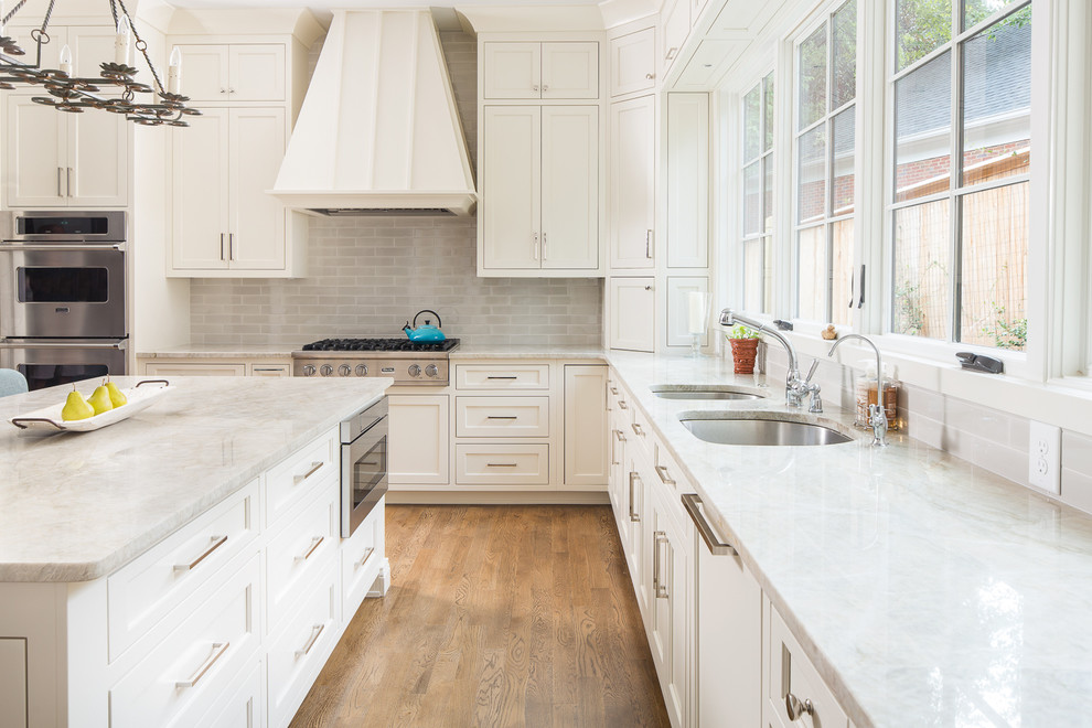 This is an example of a traditional u-shaped kitchen in Atlanta with a submerged sink, recessed-panel cabinets, white cabinets, grey splashback, metro tiled splashback, stainless steel appliances, medium hardwood flooring and an island.