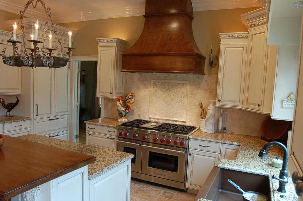 Klassisk inredning av ett mellanstort l-kök, med en rustik diskho, luckor med upphöjd panel, skåp i slitet trä, granitbänkskiva, beige stänkskydd, stänkskydd i tunnelbanekakel, rostfria vitvaror, travertin golv och en köksö