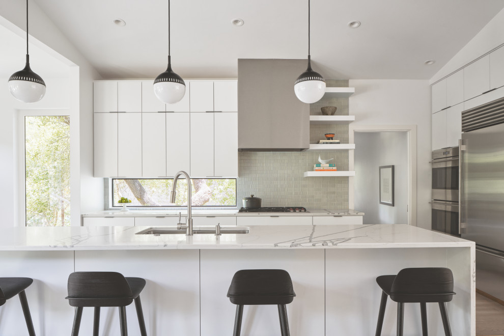 Modern inredning av ett litet vit vitt kök och matrum, med släta luckor, vita skåp, grått stänkskydd, rostfria vitvaror, ljust trägolv, en köksö och brunt golv