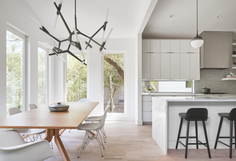 Small modern kitchen in Austin with flat-panel cabinets, white cabinets, grey splashback, light hardwood flooring, an island, brown floors, white worktops and stainless steel appliances.