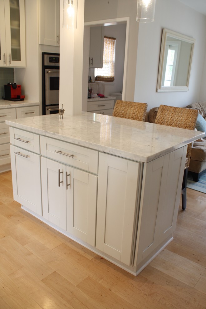 Maritim inredning av ett kök, med en enkel diskho, skåp i shakerstil, vita skåp, marmorbänkskiva, grått stänkskydd, stänkskydd i keramik, rostfria vitvaror, ljust trägolv och en köksö