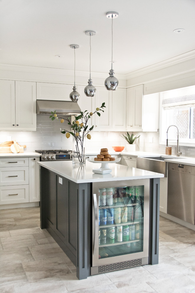 Transitional l-shaped gray floor kitchen photo in Toronto with a farmhouse sink, shaker cabinets, white cabinets, gray backsplash, glass tile backsplash, stainless steel appliances and an island