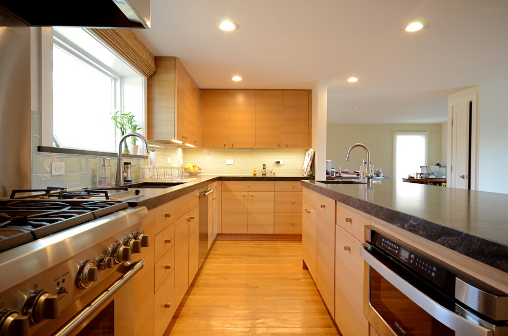 Example of a trendy l-shaped eat-in kitchen design in Boston with an undermount sink, flat-panel cabinets, light wood cabinets, granite countertops, green backsplash, subway tile backsplash and stainless steel appliances