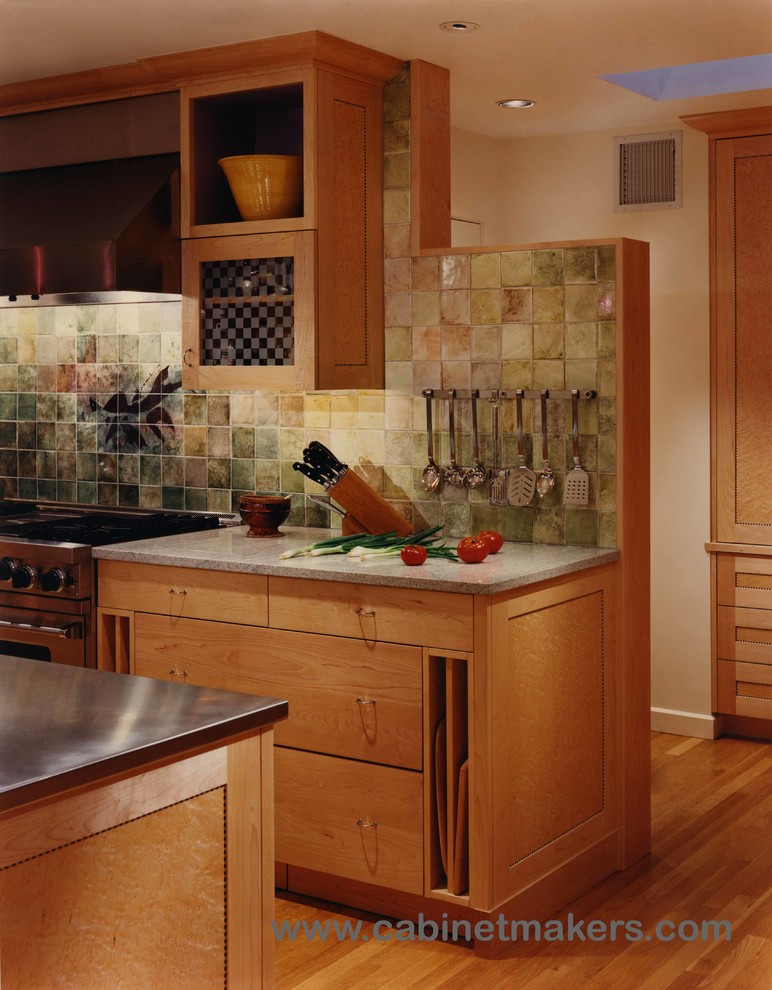 Bild på ett funkis kök, med skåp i ljust trä, stänkskydd i stenkakel och rostfria vitvaror