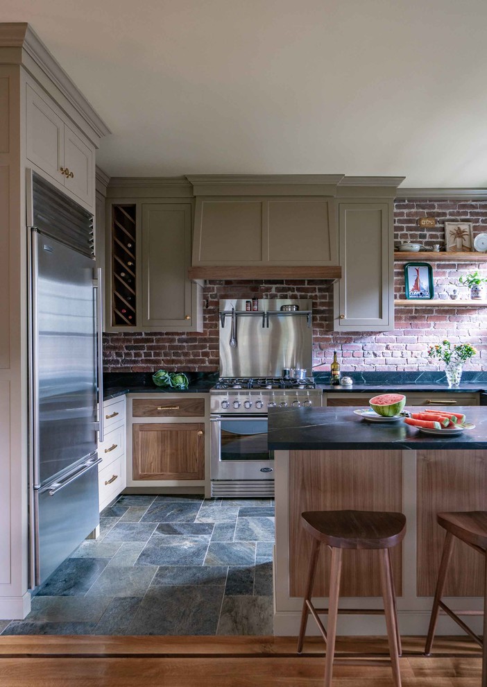 Kitchen pantry - mid-sized country l-shaped slate floor and multicolored floor kitchen pantry idea in Boston with shaker cabinets, brown cabinets, stainless steel appliances, an island, black countertops, an undermount sink, red backsplash and brick backsplash