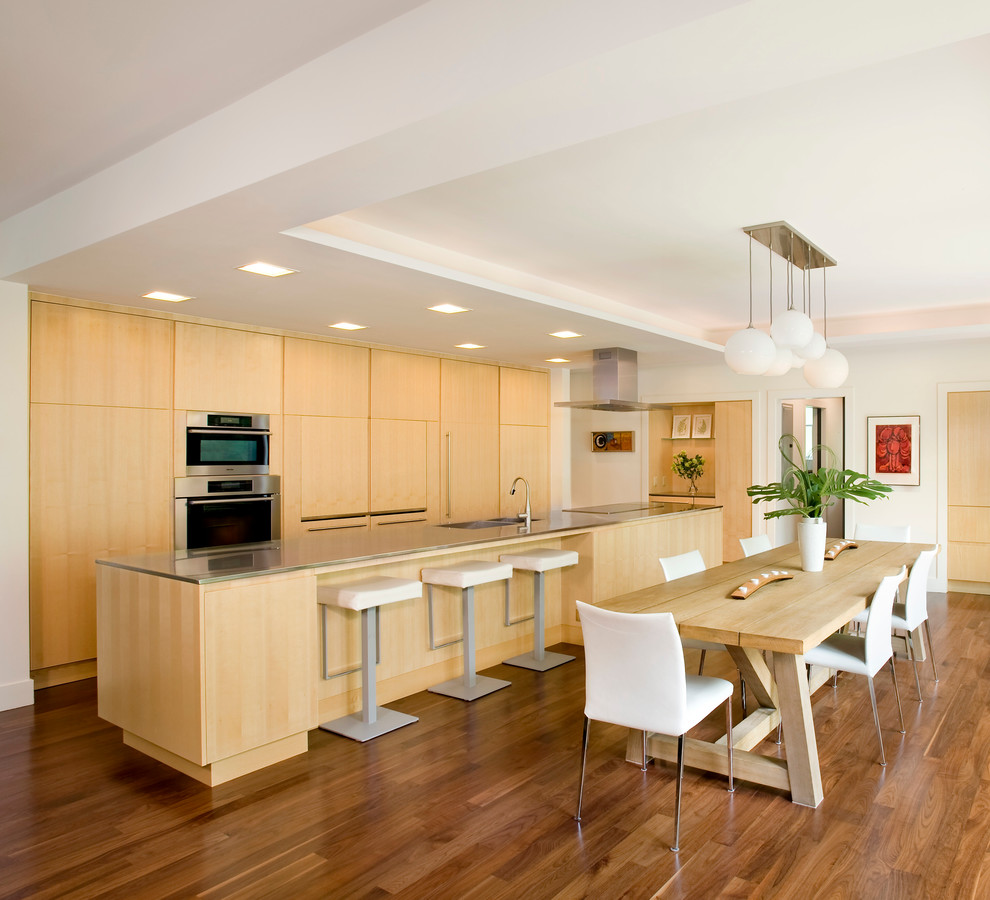 На фото: параллельная кухня-гостиная в современном стиле с плоскими фасадами, светлыми деревянными фасадами, техникой из нержавеющей стали, темным паркетным полом и островом